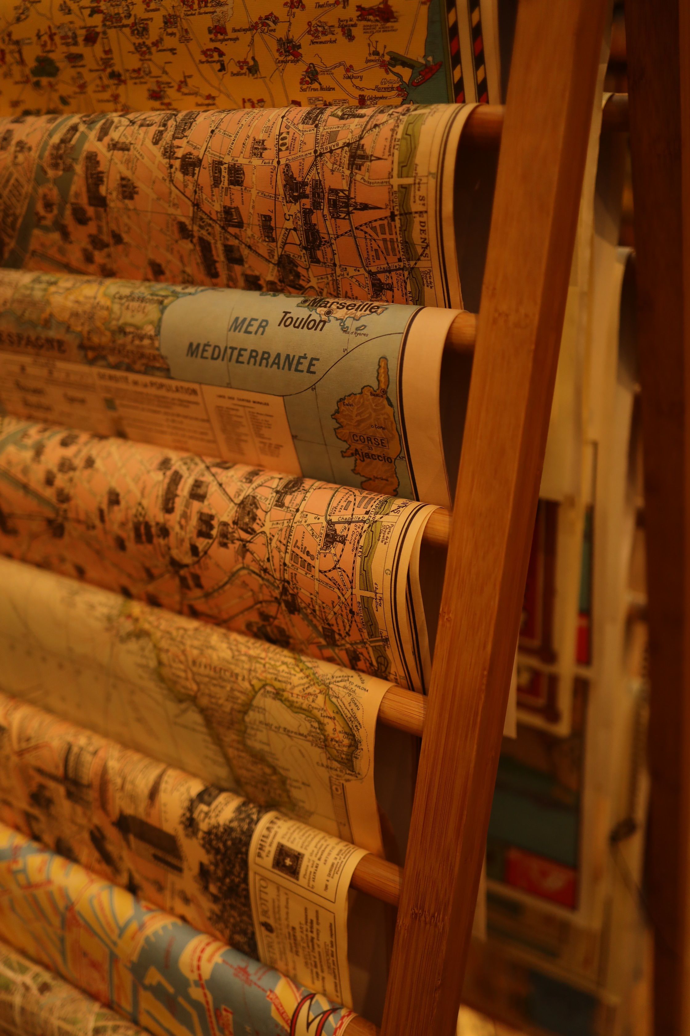 Various maps arranged neatly on a wooden rack, showcasing geographical details in warm lighting.