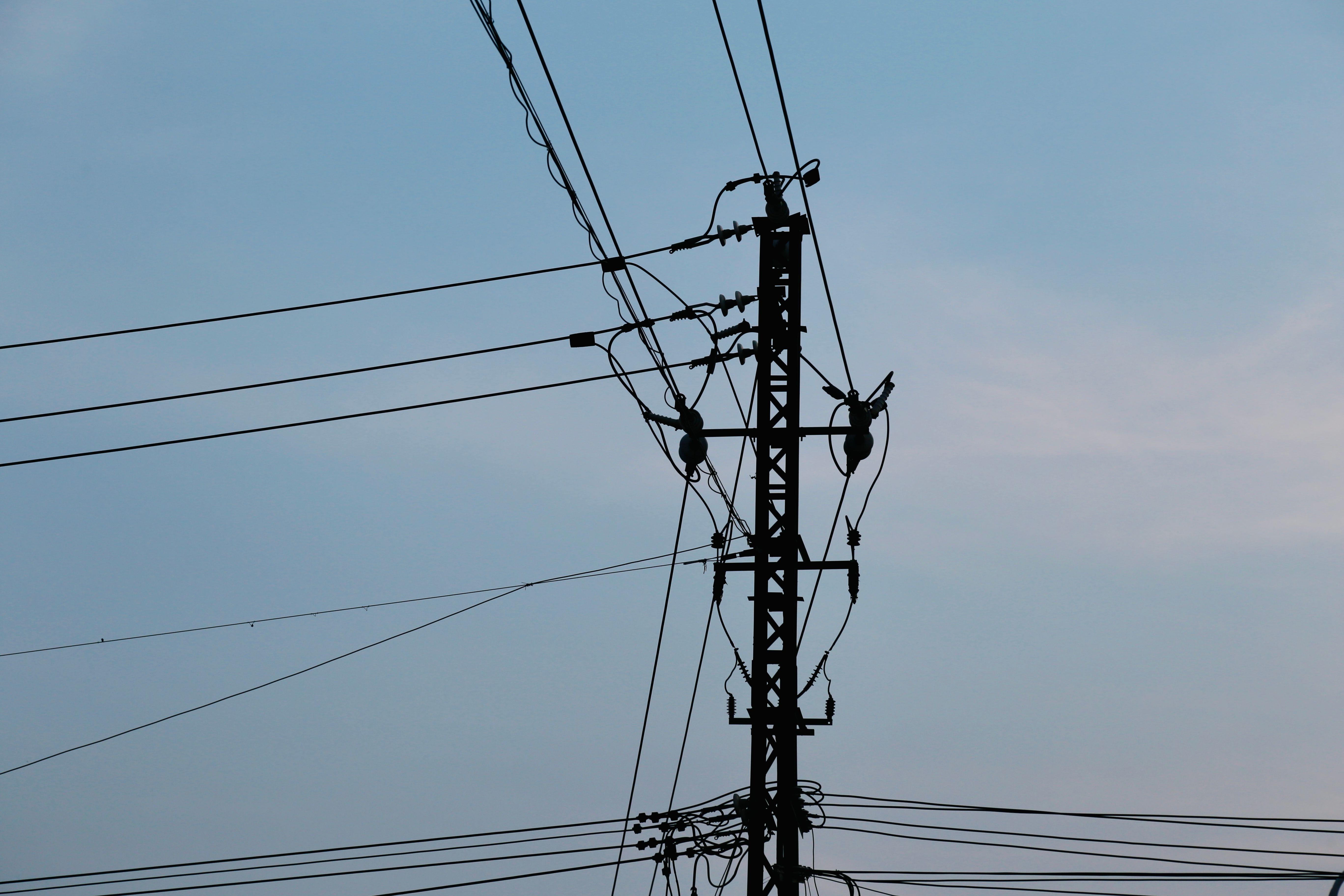 Silhouette of a utility pole with power lines against a clear blue sky, showcasing urban energy infrastructure.