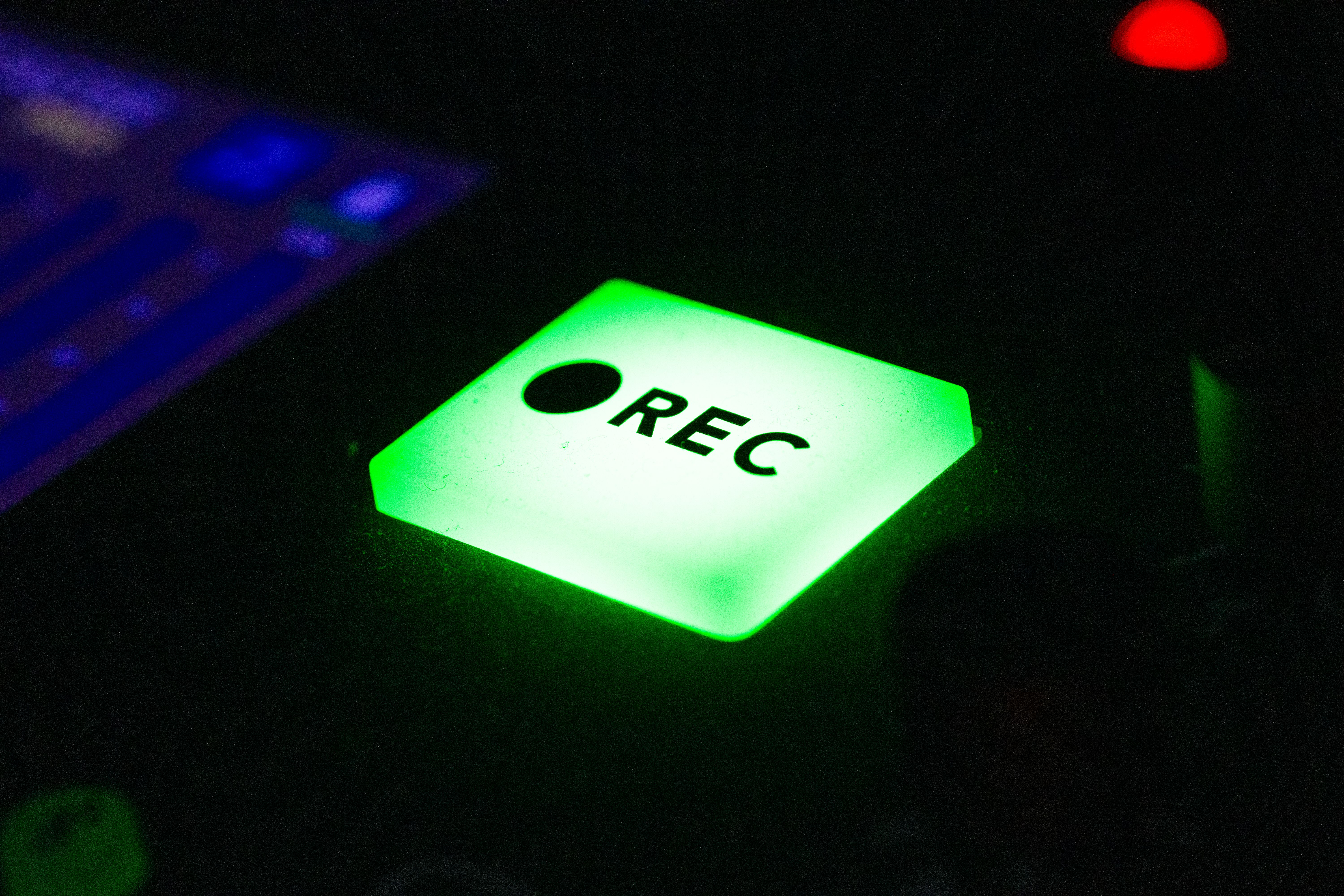 Close-up of a green illuminated recording button on electronic device in low light.