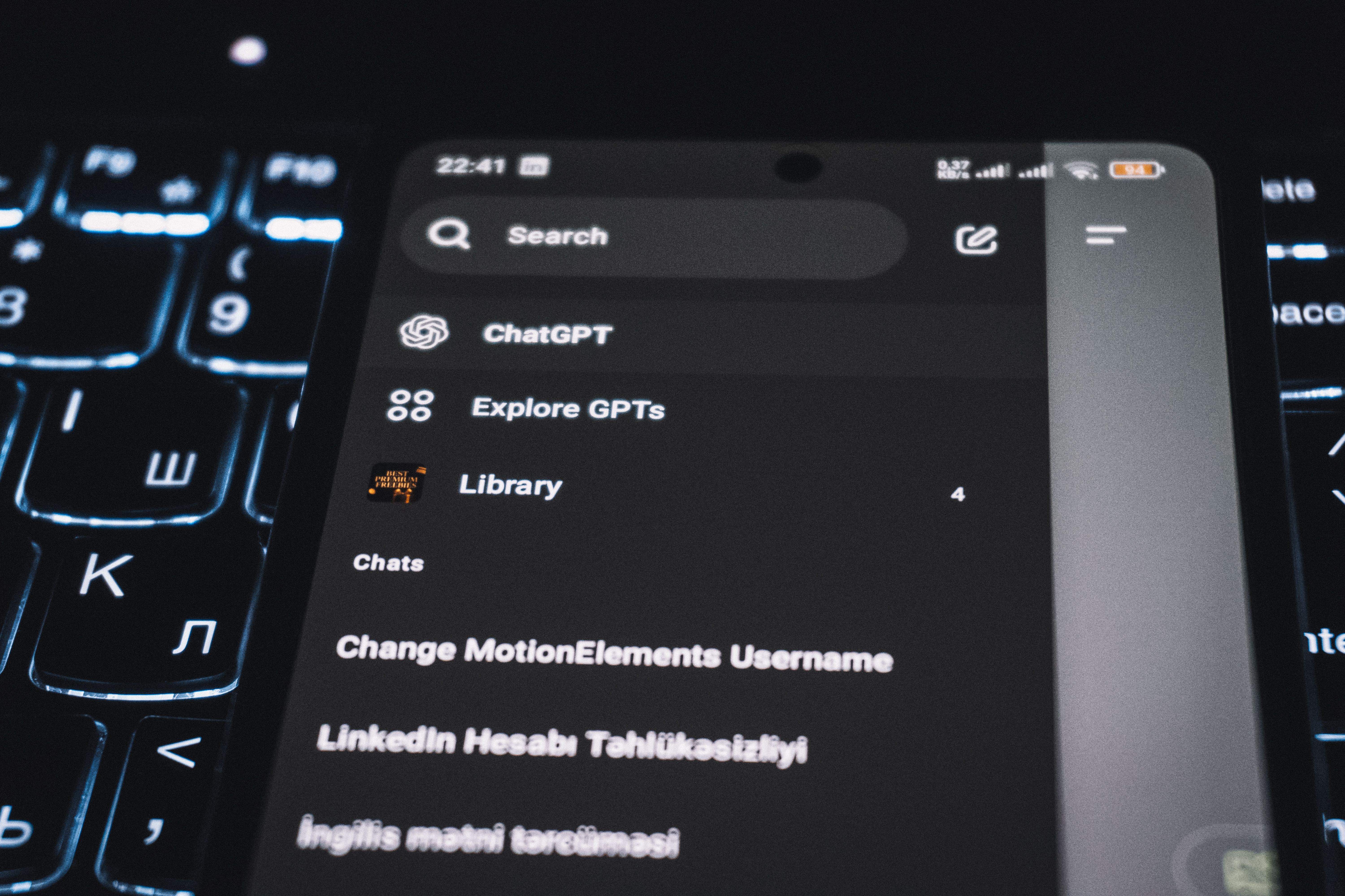 Close-up of a smartphone displaying a chat app interface with a backlit keyboard in the background.
