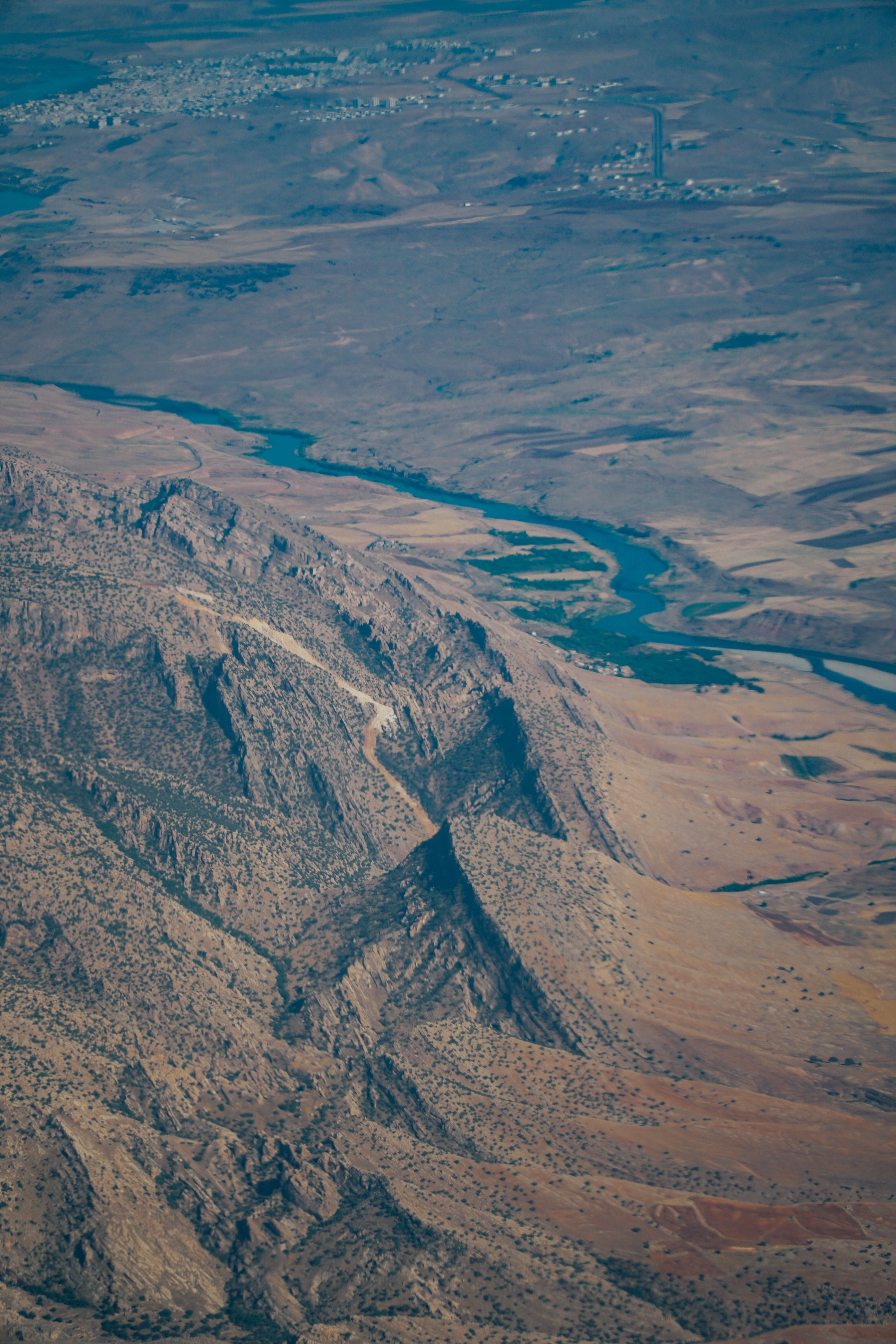 A breathtaking aerial view capturing a mountain range and winding river in an expansive arid landscape.