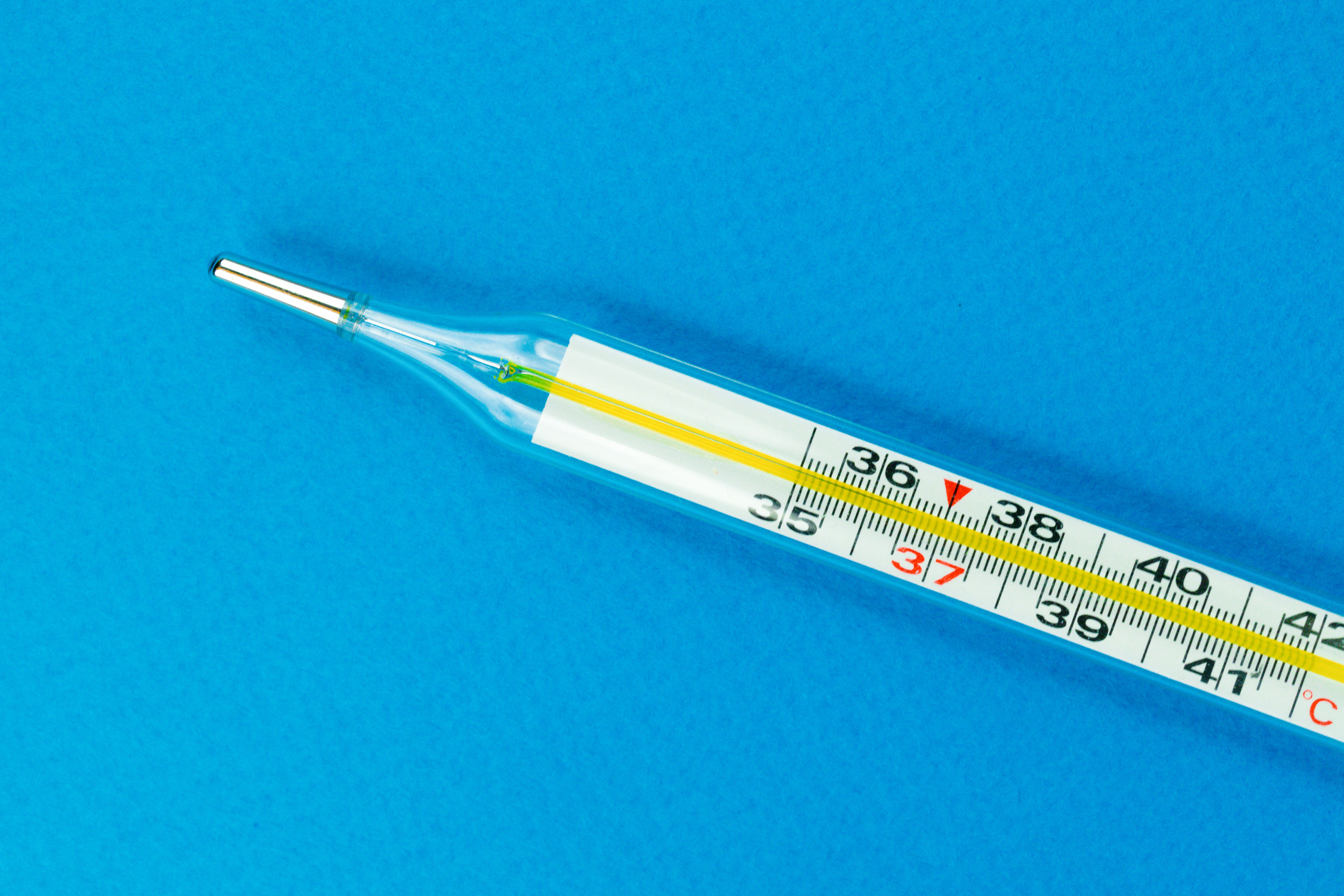 Close-up shot of a traditional glass thermometer on a vibrant blue background.
