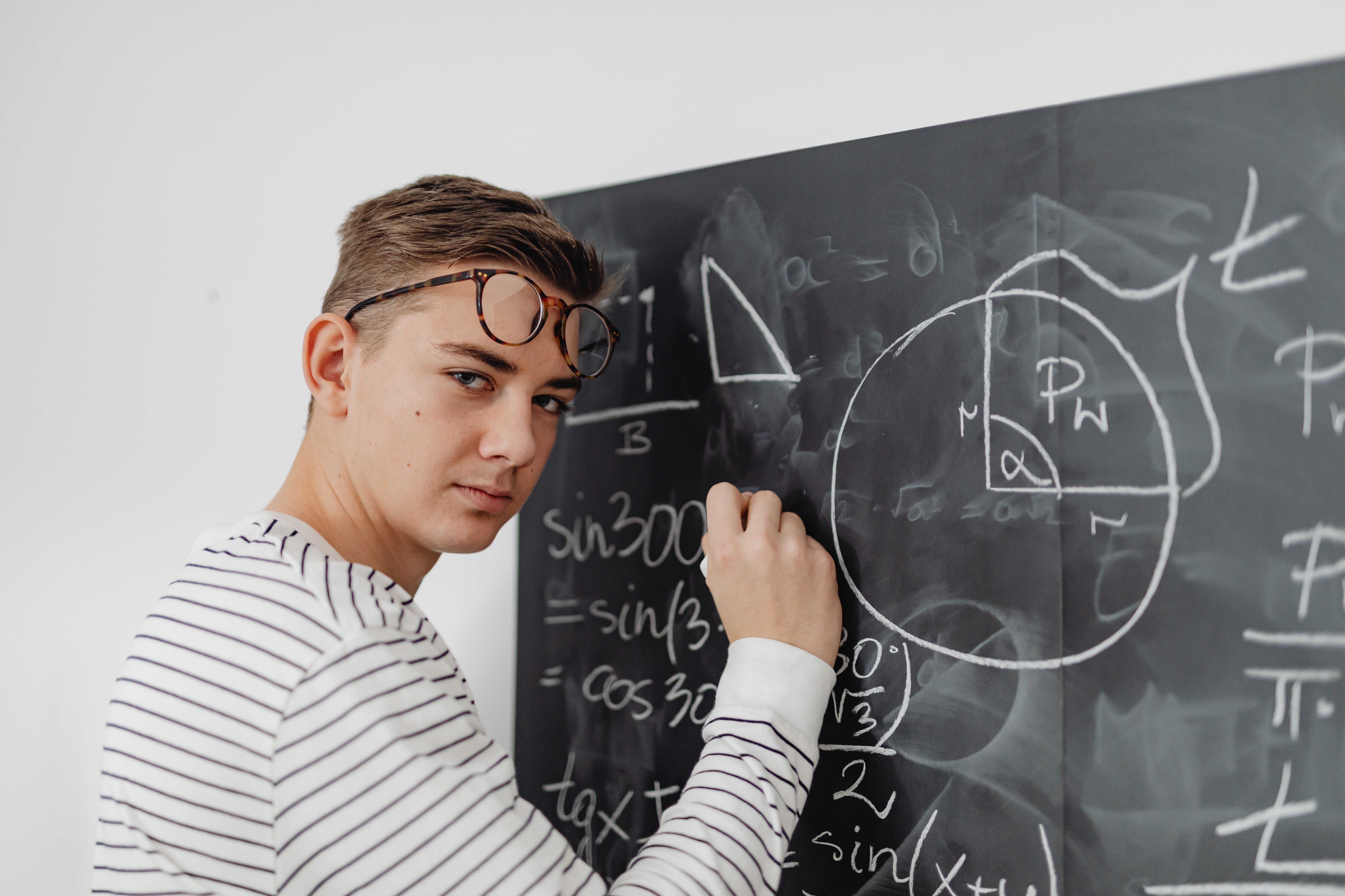 A teenager writes mathematical equations on a blackboard, focusing on geometry and trigonometry.