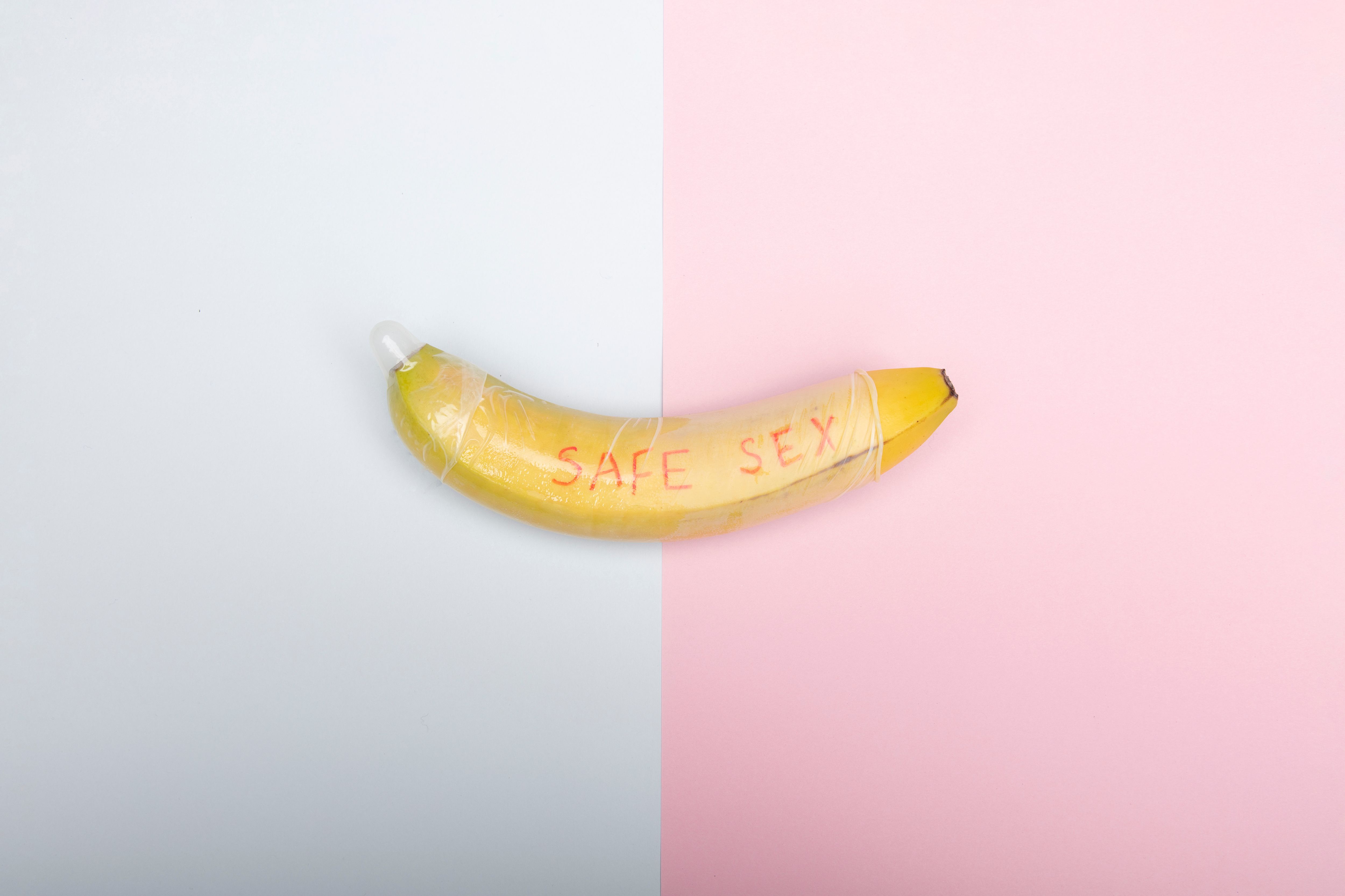 Conceptual image of a banana with condom promoting safe sex education against a pastel backdrop.