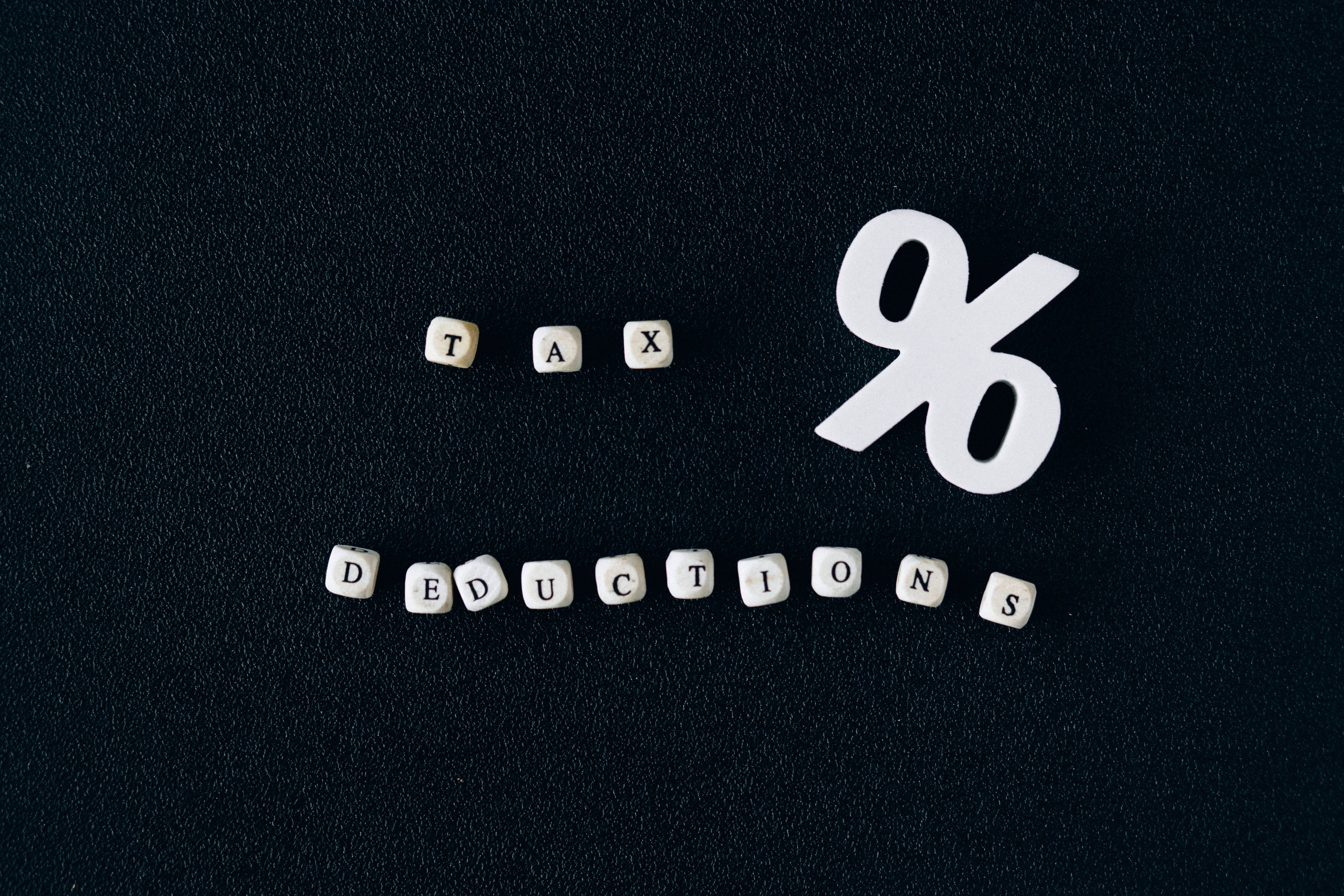 Conceptual image of tax deductions with alphabet blocks and percent symbol on black surface.