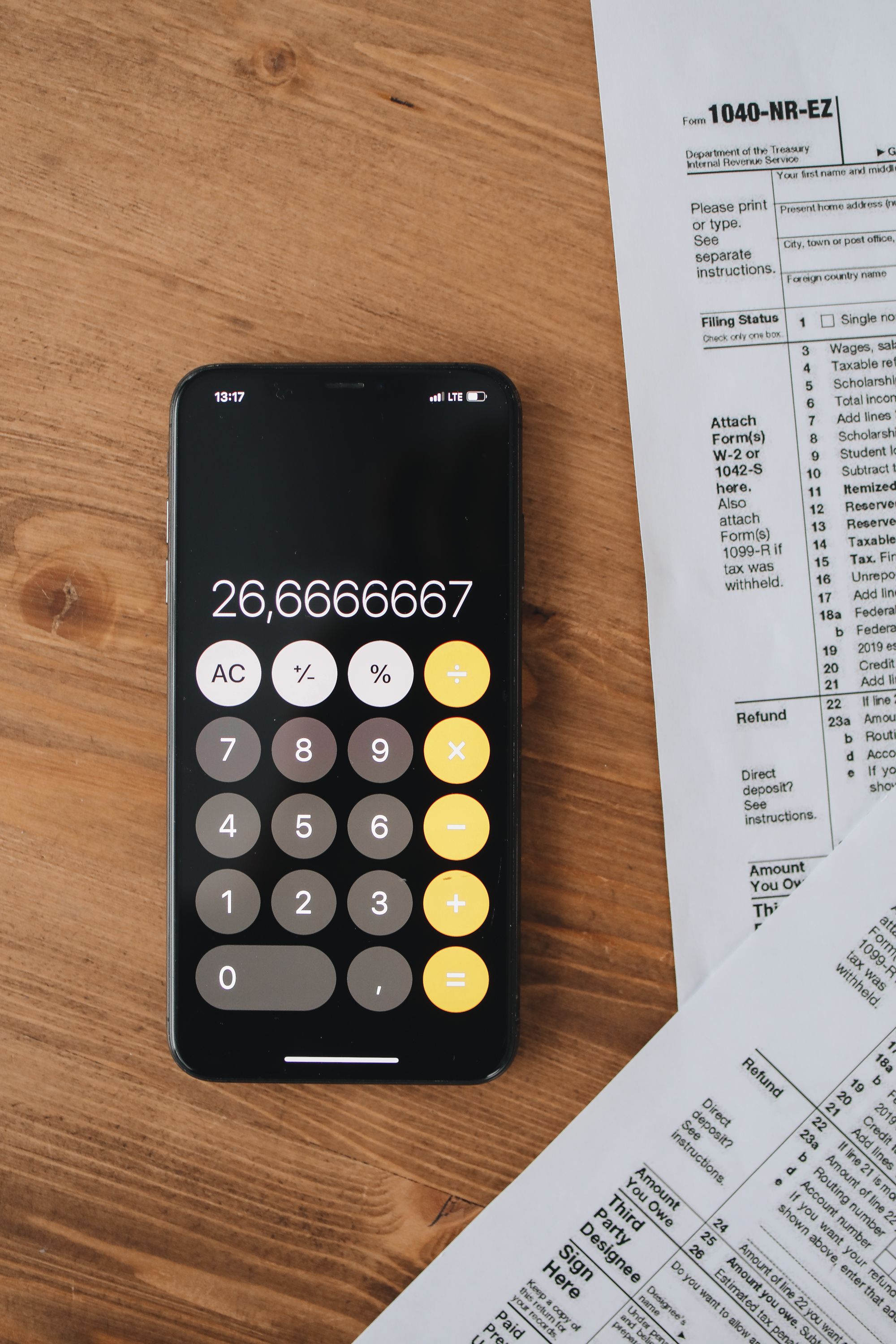 Overhead shot of a smartphone calculator displaying a number next to tax forms on a wooden surface.