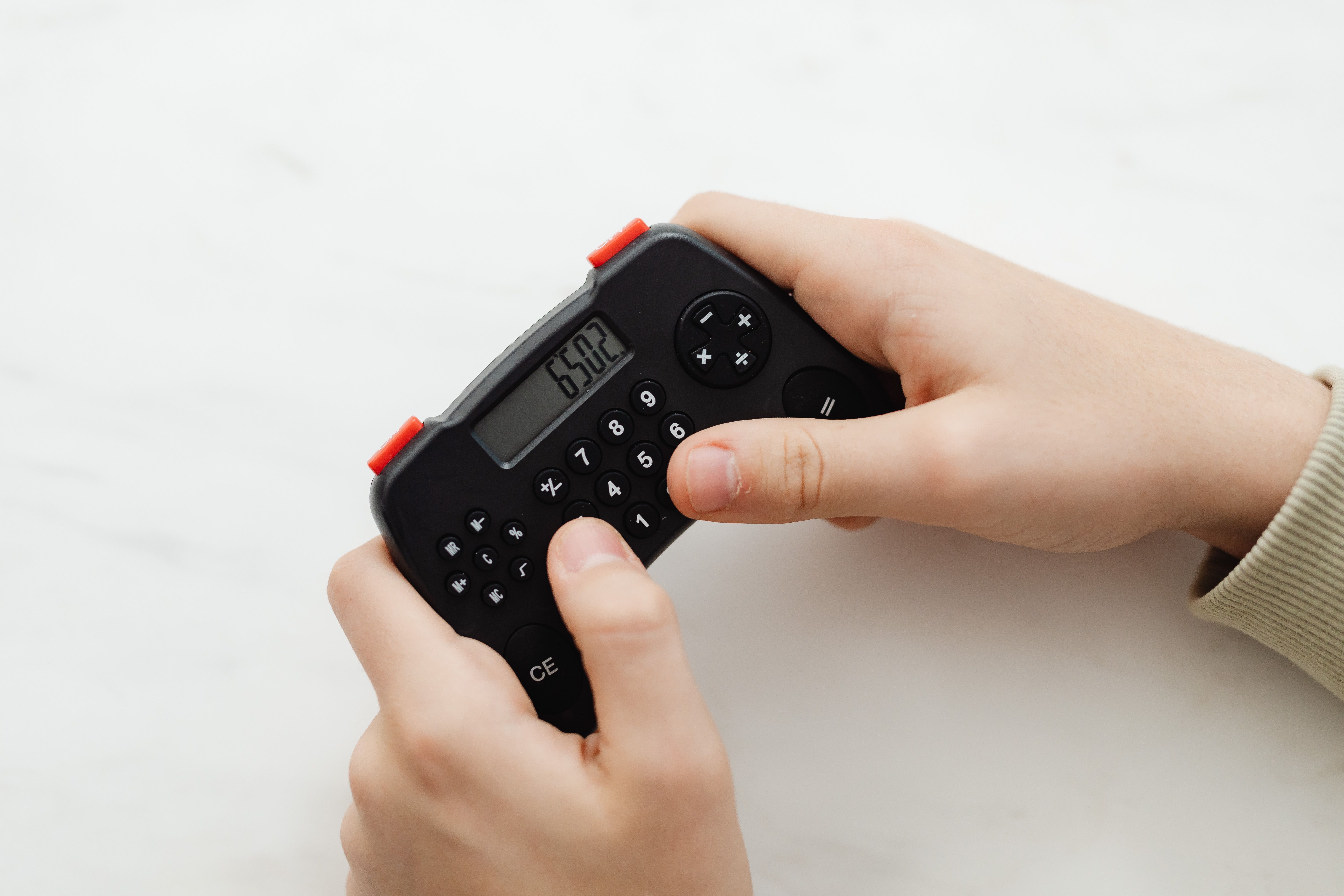 Hands holding a small black calculator displaying 6302 on a white background.