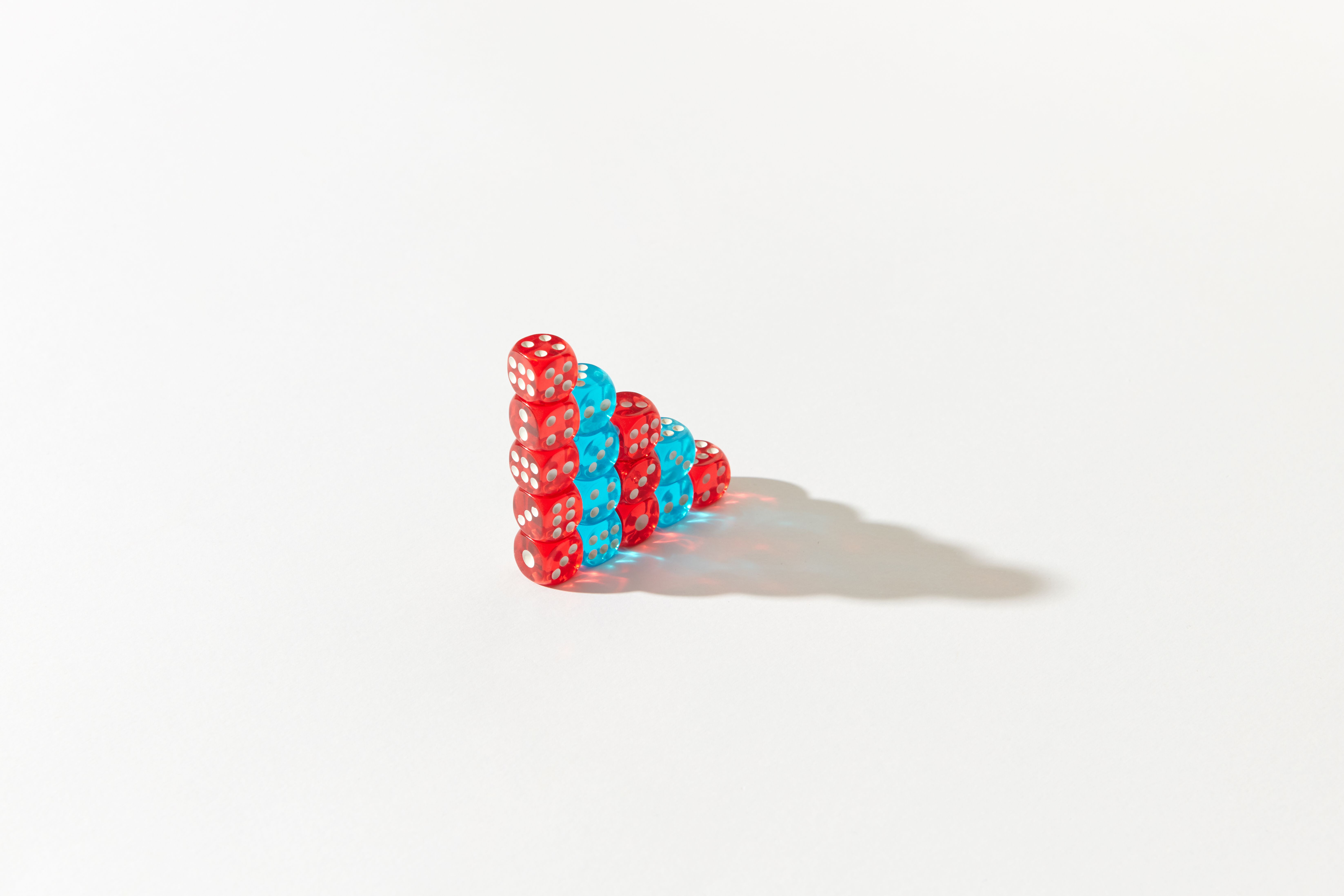 Stacked red and blue dice form a pyramid on a white background, casting a shadow.