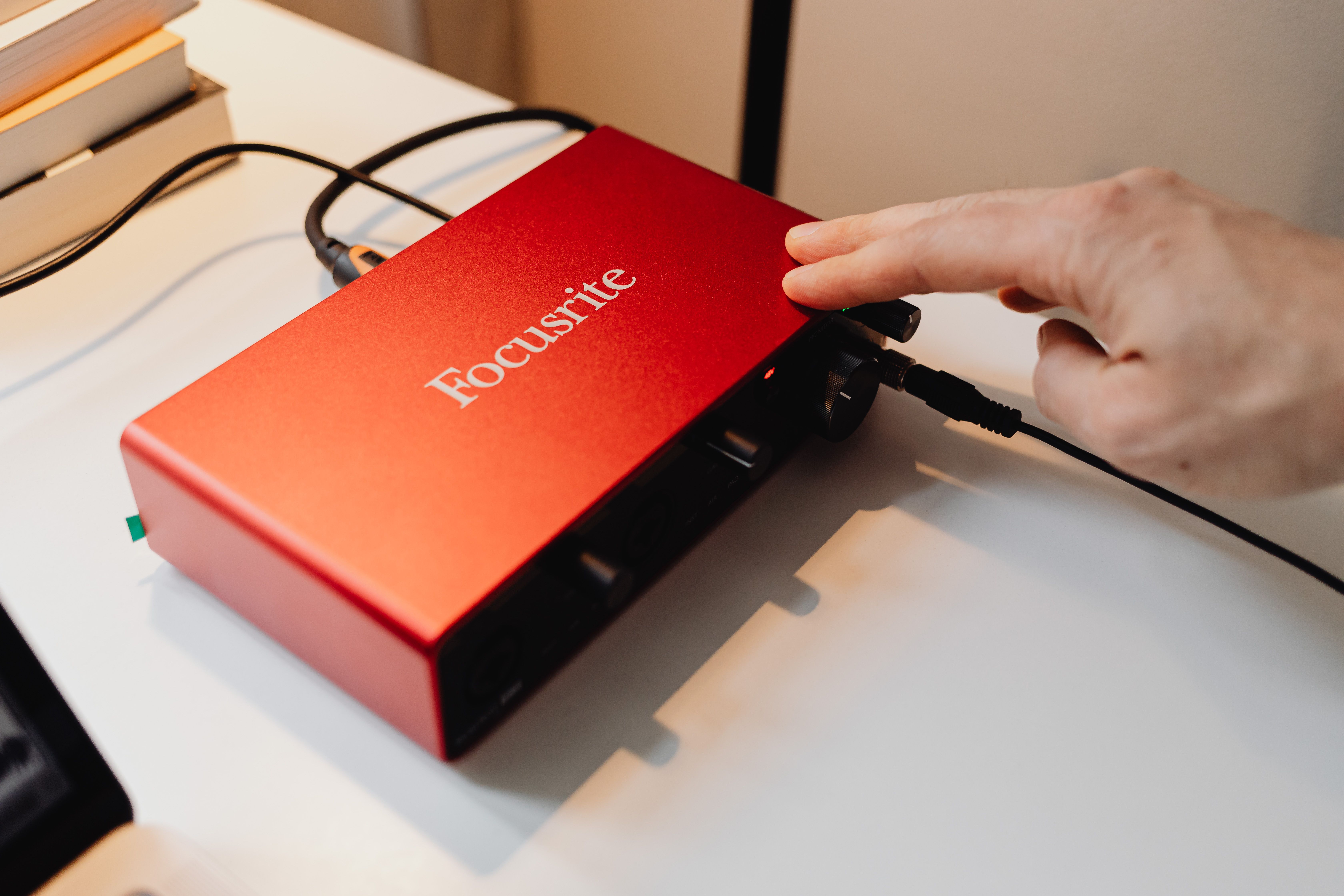Detailed view of a red audio interface being operated by a hand on a desk.