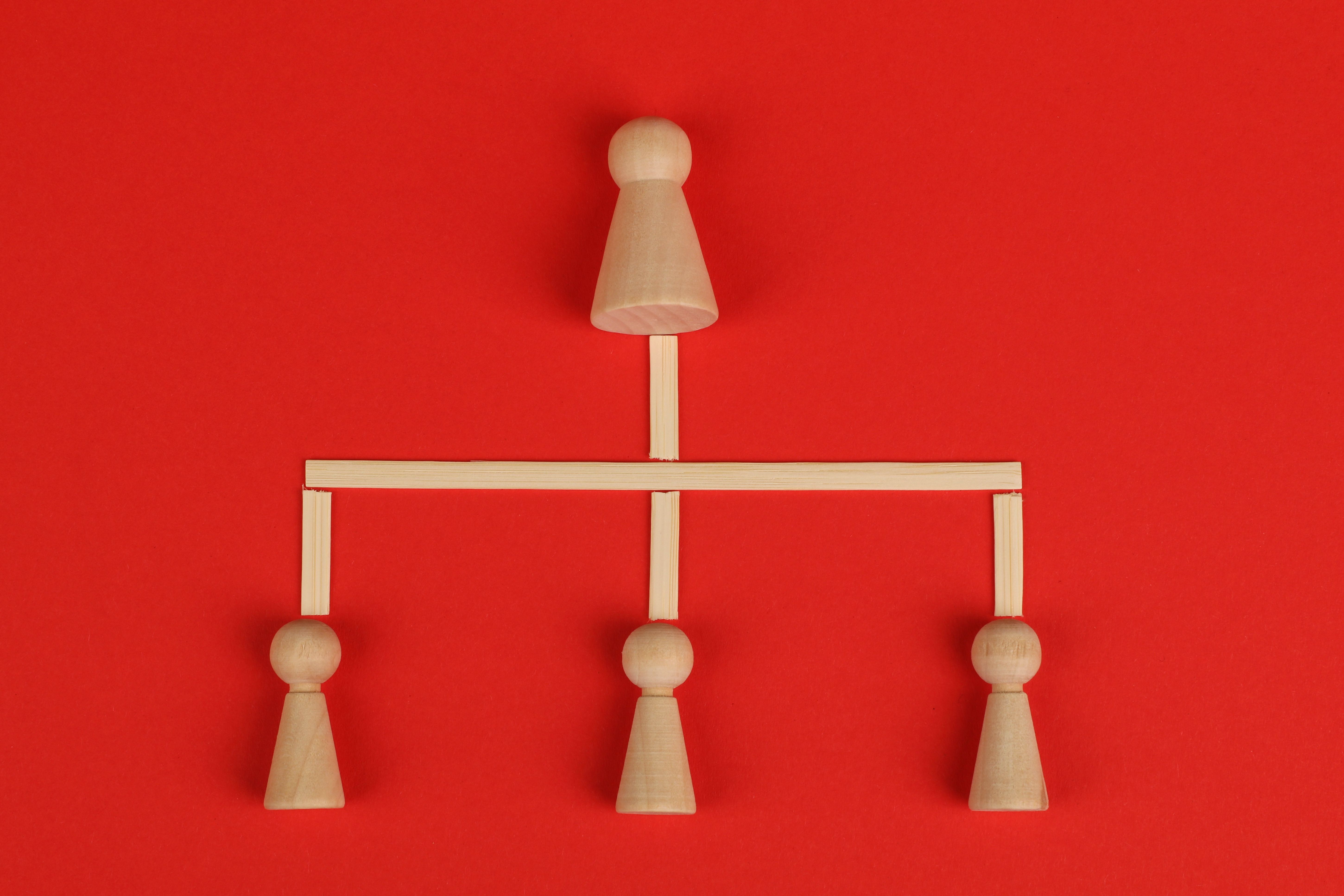 Conceptual depiction of hierarchy using wooden pieces on a vibrant red background.