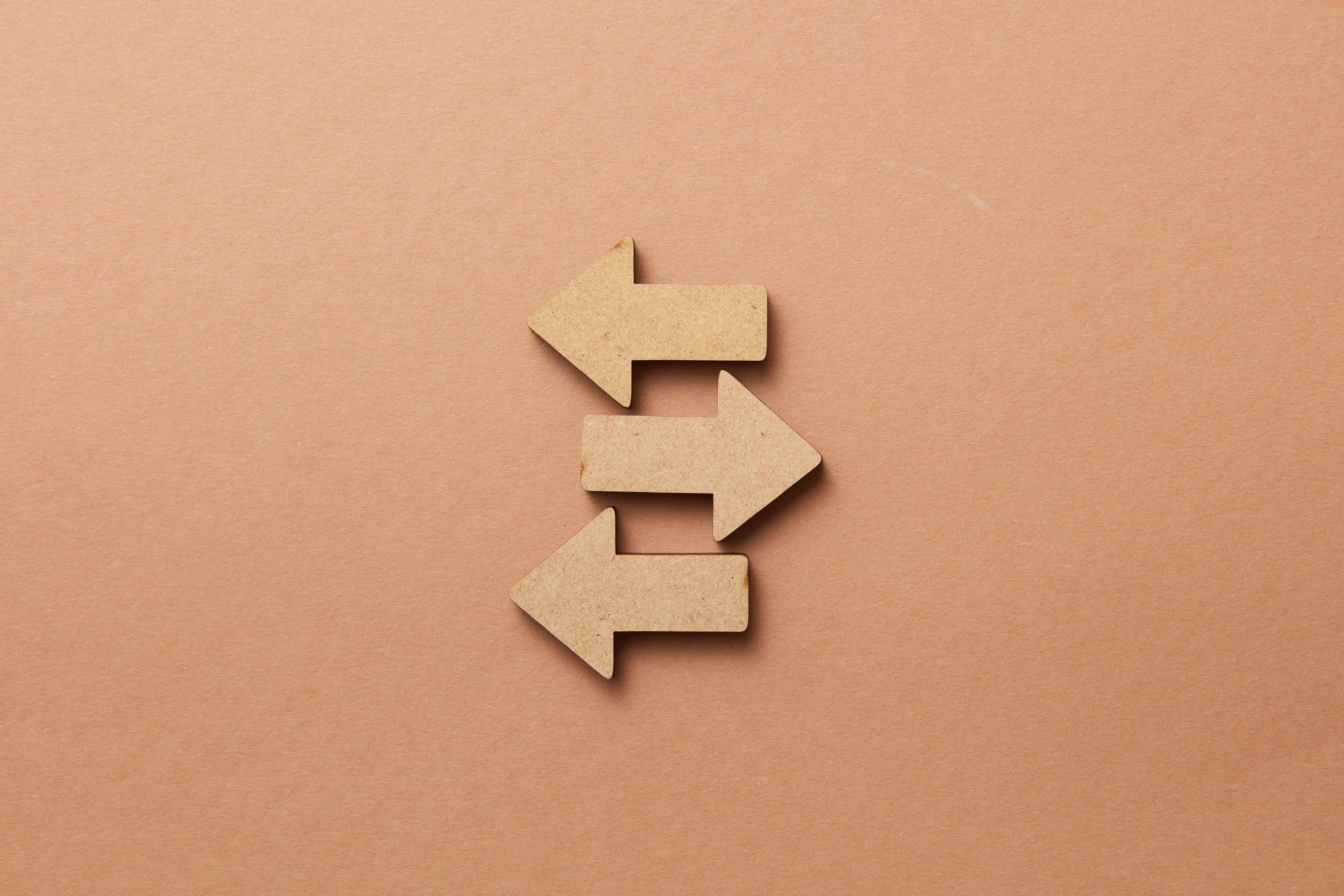 Close-up of three wooden arrows pointing in opposite directions on a beige surface.