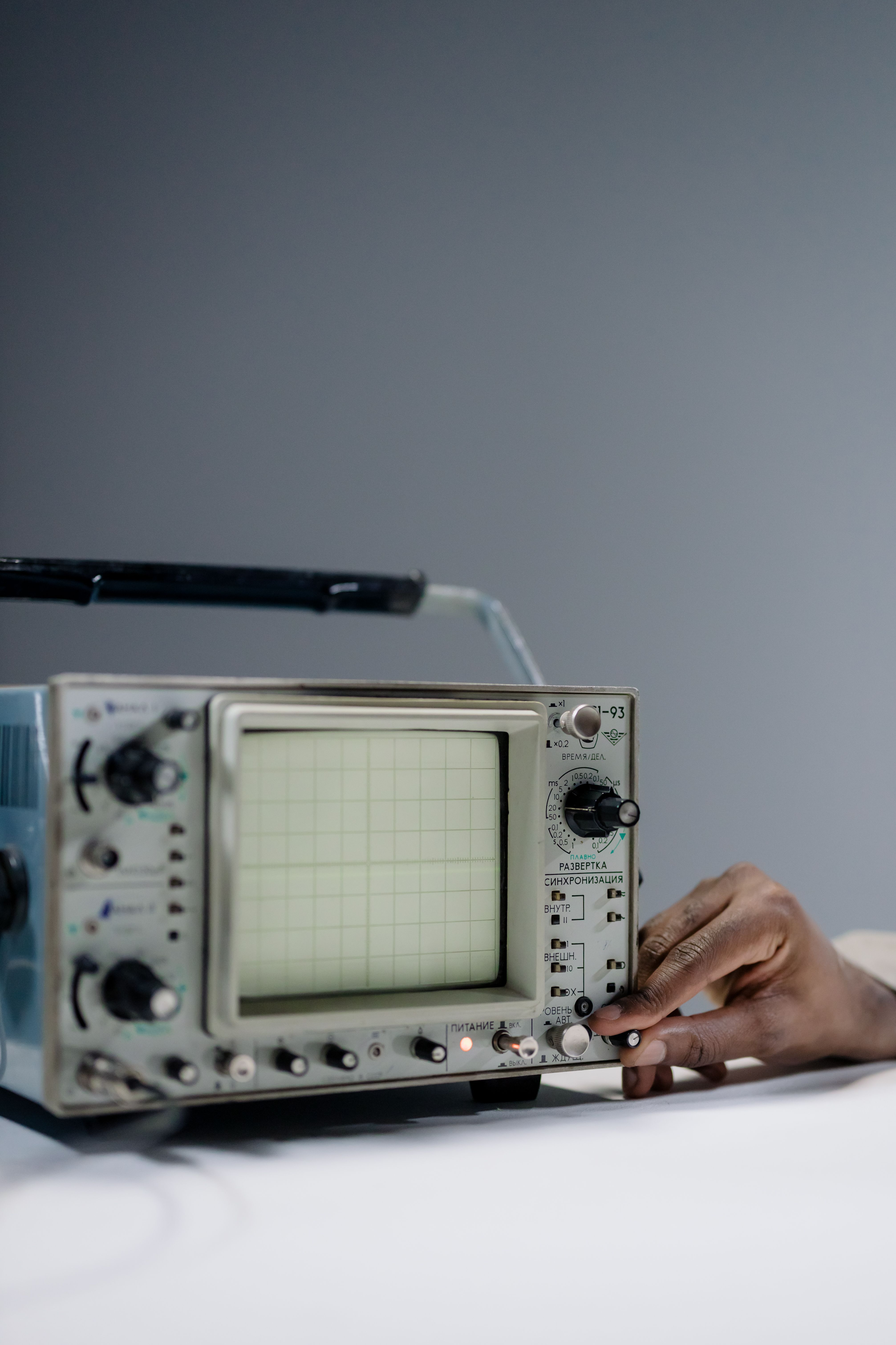 Close-up of a hand adjusting an oscilloscope knob in a laboratory environment.