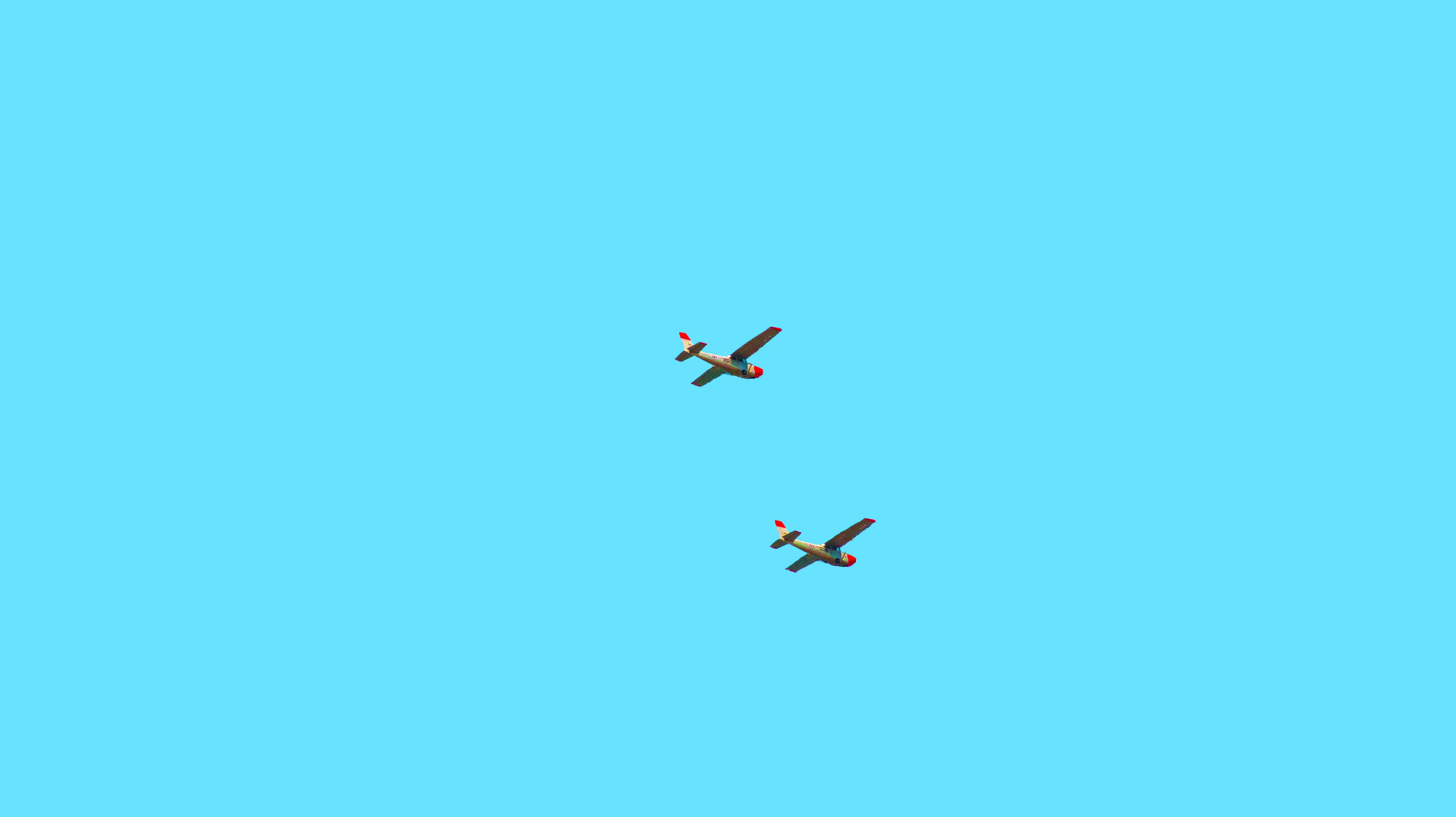 Two vintage airplanes soar against a bright blue sky, capturing serene aviation essence.