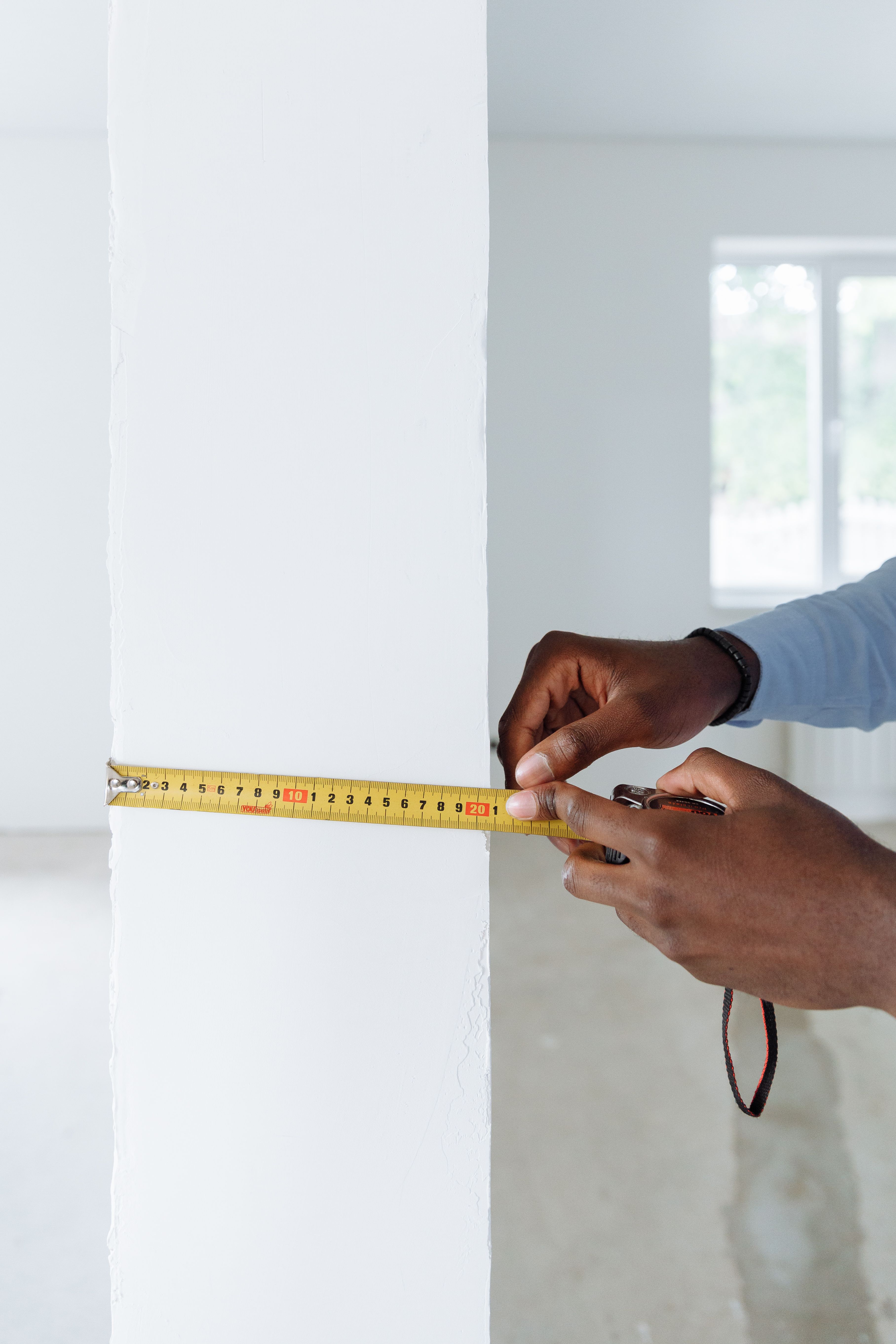 Detailed shot of hands using a tape measure against a white wall indoors.