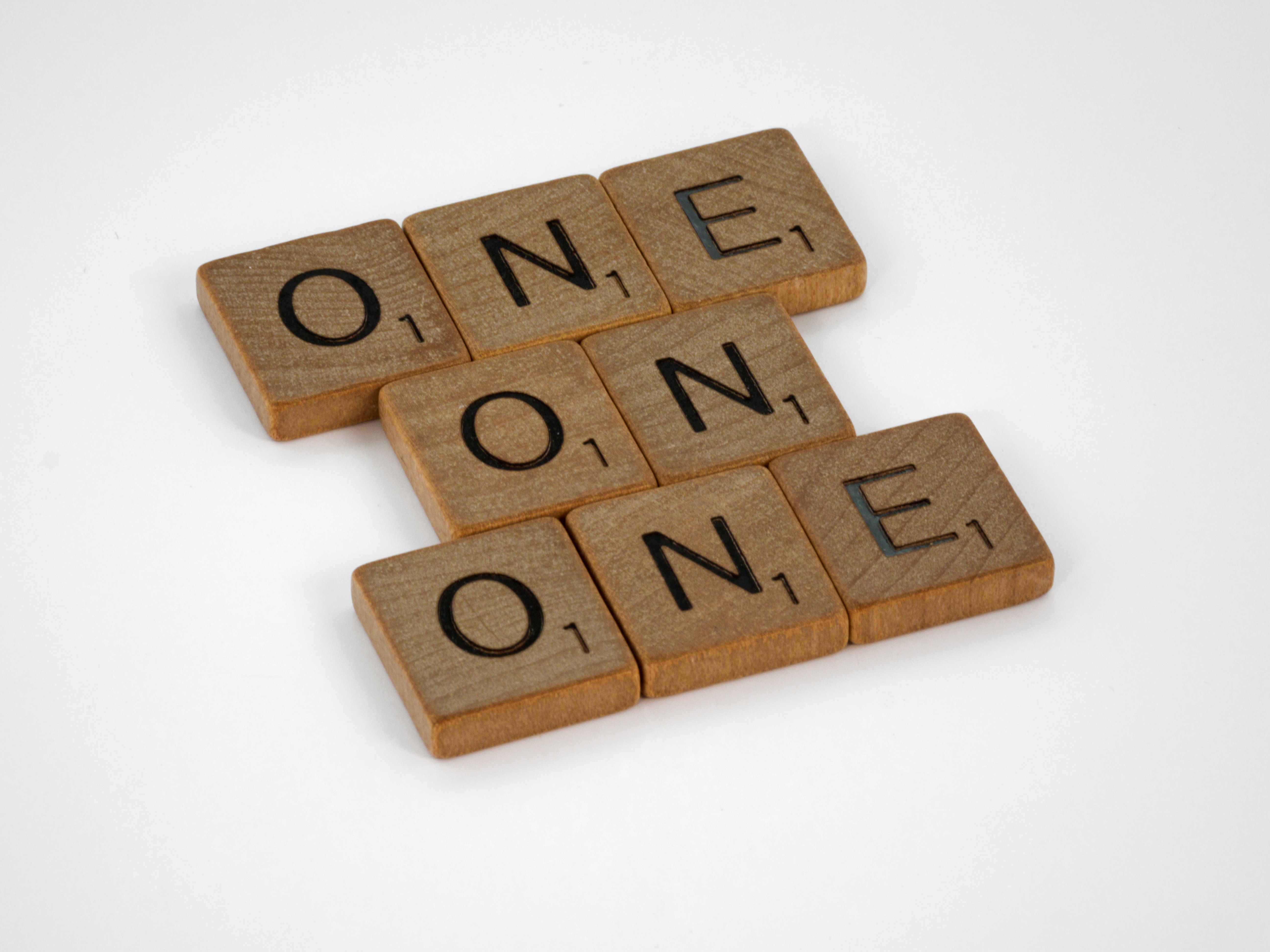 Scrabble letter tiles arranged to spell 'ONE' in a crossword style on a white background.
