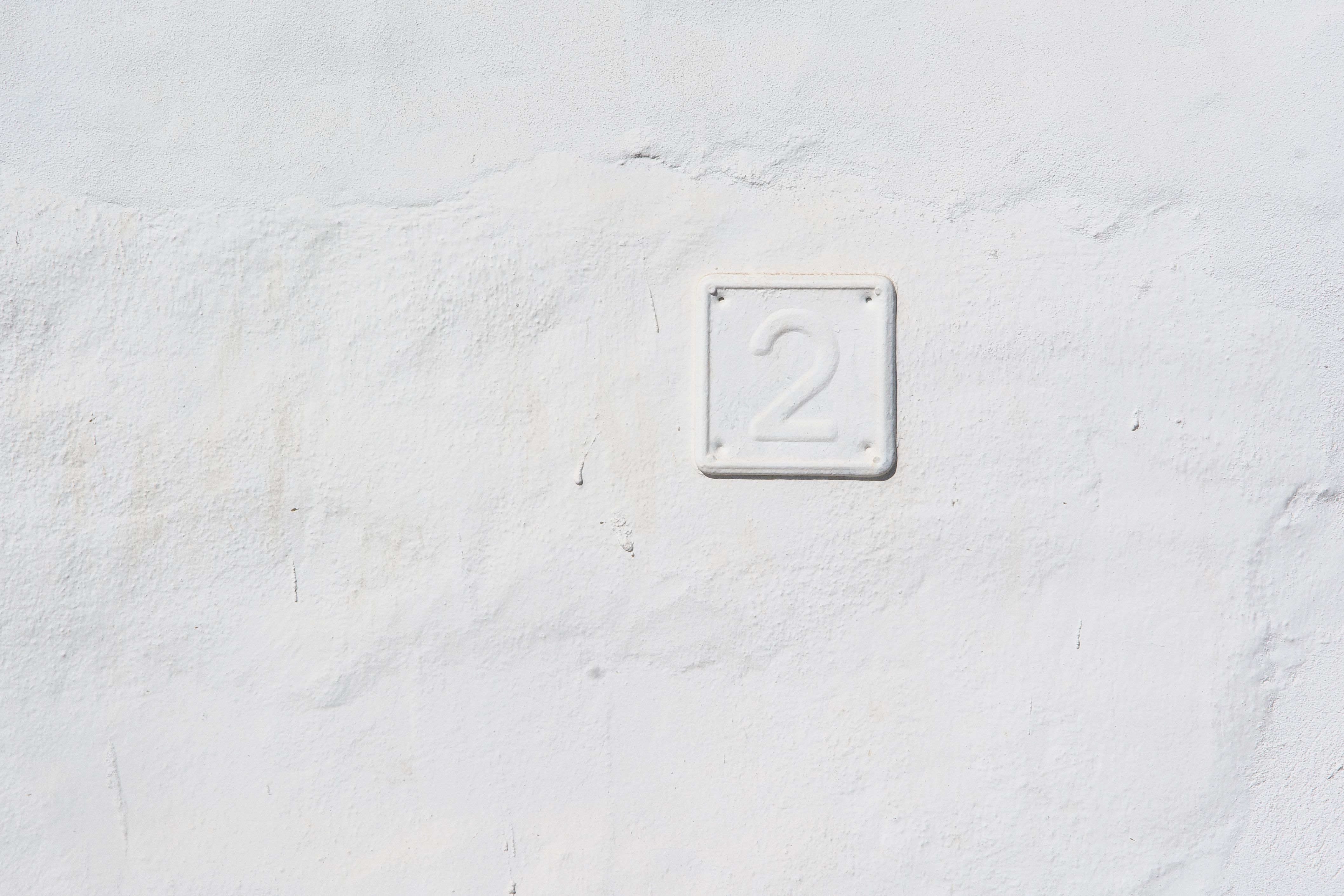 Monochrome texture featuring the number two embossed on a white wall.