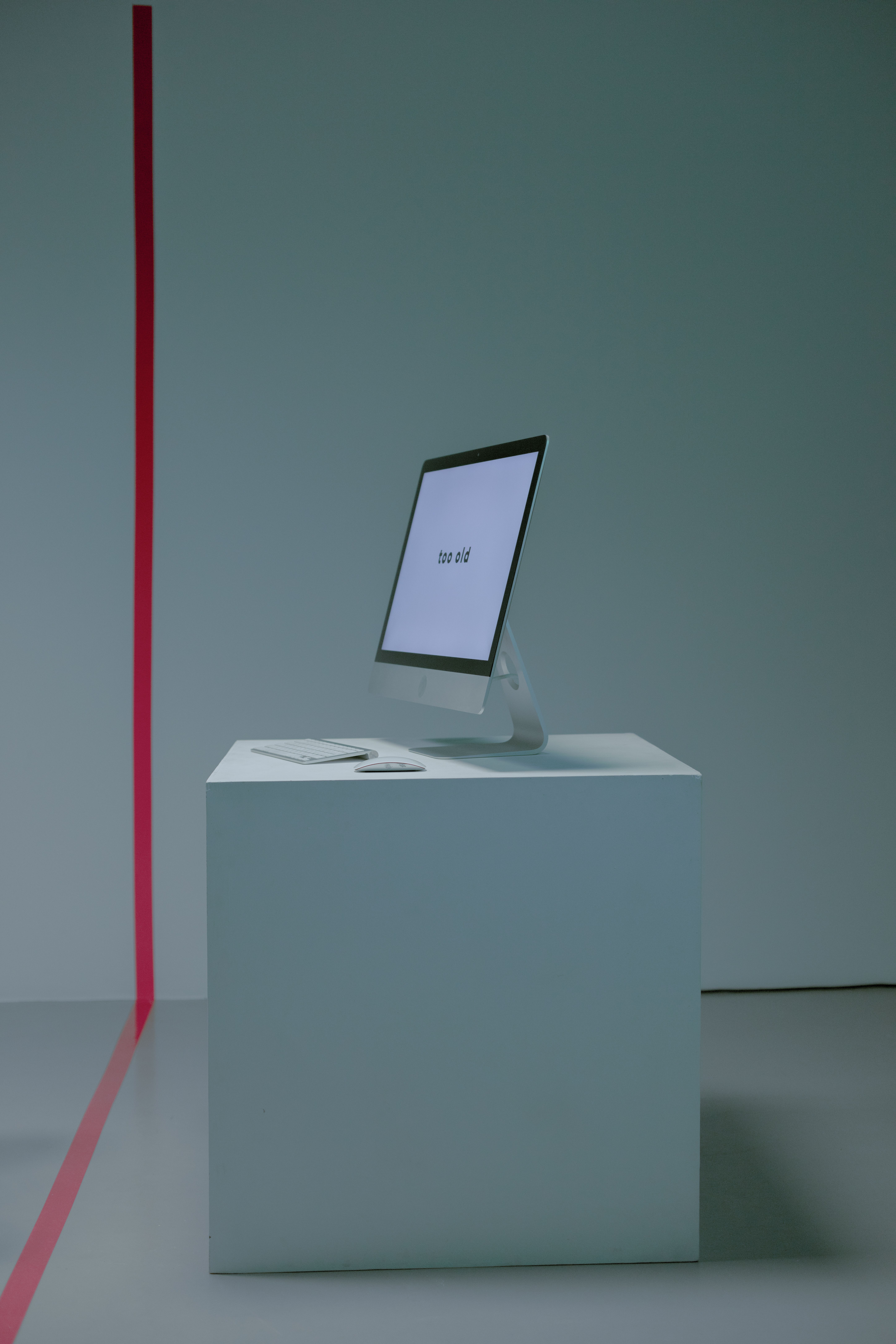A minimalist computer setup on a white podium with red line in a studio environment.